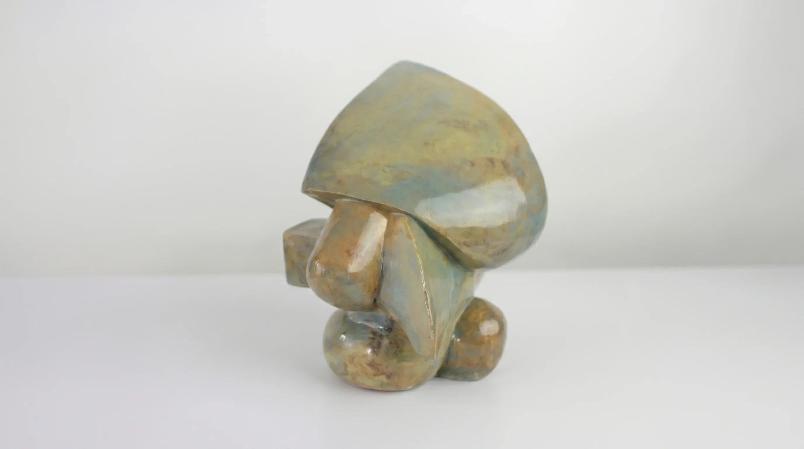 Ceramic sculpture of a mask, shiny marble green brown glaze, standing against white wall